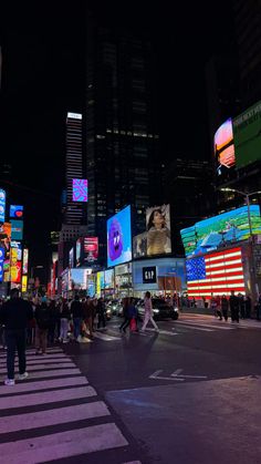 people are crossing the street at night in times square, with billboards lit up