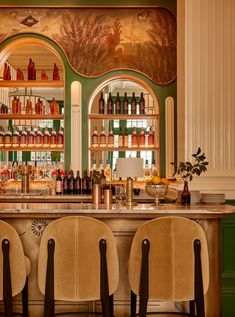 a bar with chairs and bottles on the shelves in front of two large arched windows