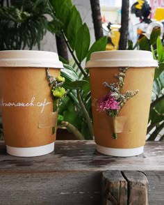 two coffee cups sitting on top of a wooden table next to each other with flowers in them