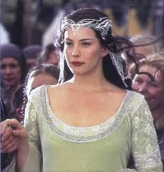 a woman in a green dress and headdress walking down the street with people behind her