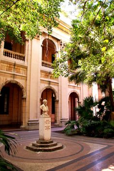 an old building with a statue in the center surrounded by greenery and palm trees