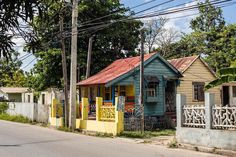 a small blue house sitting on the side of a road next to a fence and trees