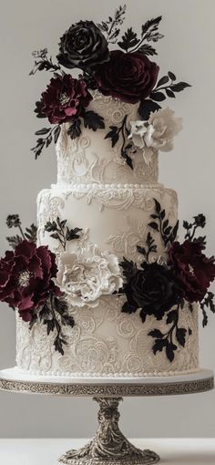 a three tiered wedding cake with black and white flowers on the top, sitting on a silver pedestal