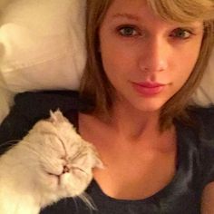 a woman laying in bed with a cat on her arm and looking at the camera