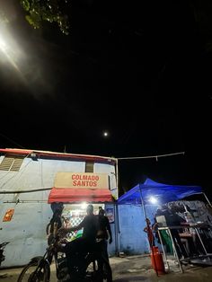 two people standing next to each other in front of a blue building with a red awning