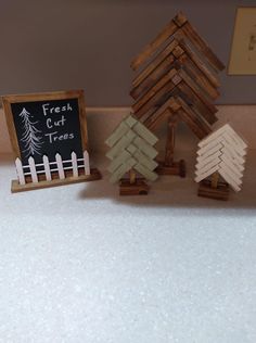 three wooden christmas trees sitting next to a chalkboard on a counter top in front of a sign that says fresh cut trees
