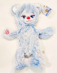 a blue teddy bear with red nose and paws on it's chest, sitting next to a white background