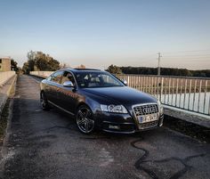 a black car parked on the side of a road next to a fence and water