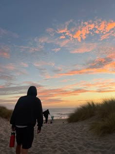 a man walking on the beach at sunset with his back to the camera, carrying a water bottle