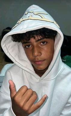 a young boy wearing a white hoodie and pointing at the camera with his finger