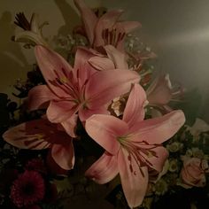 some pink flowers are in a vase with other flowers on the wall behind them and one is blurry
