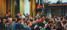 a large group of people sitting in front of a stage with one person standing up