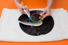 a person is using scissors to cut the vinyl record on an orange table top with a white towel