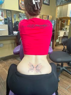 a woman sitting in a chair with her back turned to the camera and tattoos on her stomach