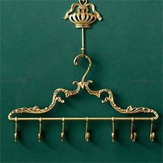 an ornate gold coat rack with hooks on it's sides and a green wall behind it