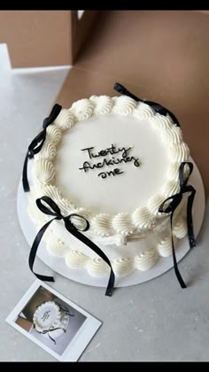a white cake with black ribbon and writing on it sitting on a table next to a photo