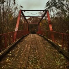 an old rusty red bridge in the middle of autumn with leaves on the ground and trees around it