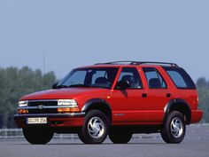 a red pick up truck parked on top of a parking lot with trees in the background