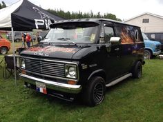 an old black van parked on top of a lush green field next to other cars