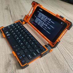an orange and black tablet sitting on top of a wooden table next to a keyboard
