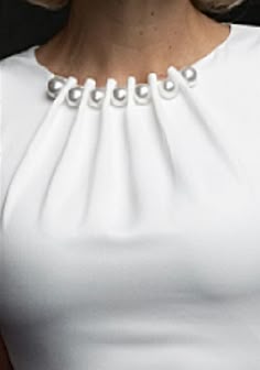 a woman with blonde hair wearing a white dress and pearls on her collar is looking at the camera