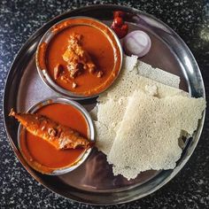 some food is on a metal plate with bread and sauces in small bowls next to each other