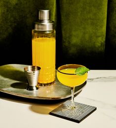 a drink sitting on top of a metal tray next to a shaker and glass
