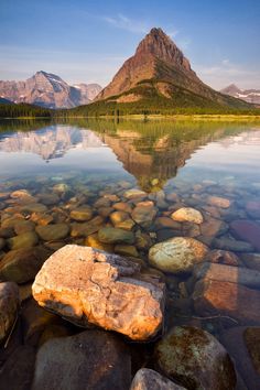 a lake with rocks in the water and mountains in the background