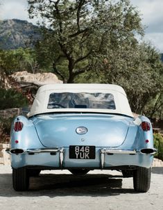 an old blue car parked in front of a tree