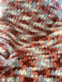 an orange, white and blue crocheted blanket laying on top of a bed