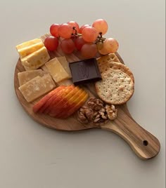 a wooden cutting board topped with cheese, crackers and fruit on top of it