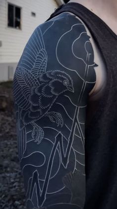 a man wearing a black shirt with white ink on his arm and shoulder is standing in front of a house