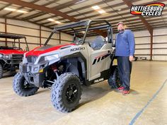 a man standing next to a red and gray polar bear utility vehicle in a garage