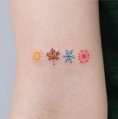 three different colored leaves on the side of a woman's arm, one with an orange sun and one with a red maple leaf