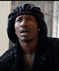 a man wearing a black hat and looking off to the side in front of a window