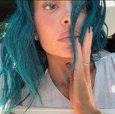 a woman with blue and green hair holding her hand to her face while sitting in a car
