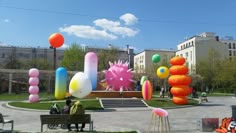 people are sitting on benches in the middle of a park with balloons floating above them