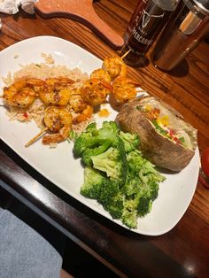 a white plate topped with shrimp, broccoli and rice next to a potato