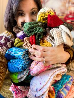 a woman is holding a large pile of knitted sweaters and scarves in her hands