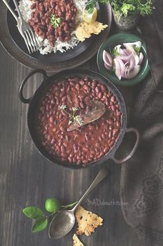 beans and rice in a bowl with spoons on a table next to other foods
