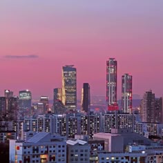 the city skyline is lit up at night with skyscrapers in the foreground and pink sky