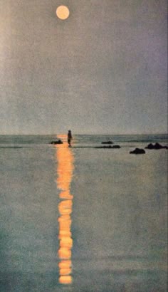 a person standing in the water at night with the moon shining brightly over the ocean
