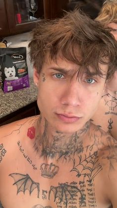 a man with lots of tattoos on his chest looking at the camera while standing in front of a counter