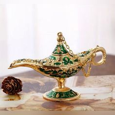 a gold and green teapot sitting on top of a table next to a pine cone