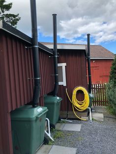 two large green barrels sitting next to each other on top of a gravel road near a red building
