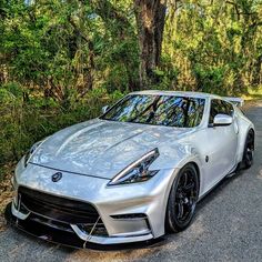 a silver sports car parked on the side of a road in front of some trees