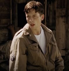 a young man is standing in front of an old wooden building and looking at the camera