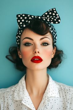 A woman with vintage-style makeup and a polka dot headband poses against a teal background. Her makeup includes bold red lipstick, winged eyeliner, and rosy cheeks, embodying a classic 1950s beauty look. She wears a white blouse with black polka dots, matching her hair accessory