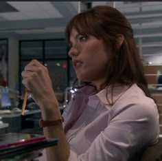 a woman sitting at a desk with a pen in her hand and looking off to the side