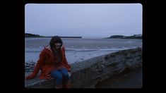 a woman sitting on the edge of a stone wall next to an ocean and beach